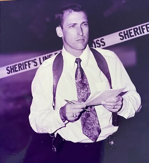 Randy Ball as a Major Crimes detective, holding a notepad in front of a 'Sheriff's Line — Do Not Cross' tape.