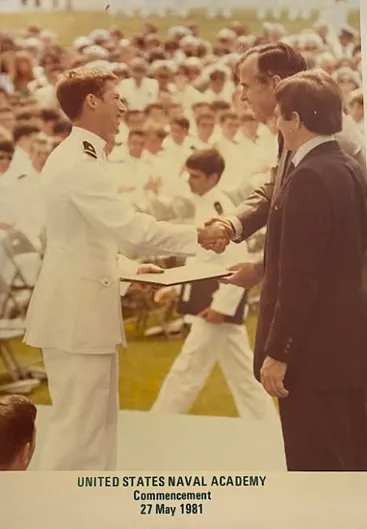Randy Ball at his United States Naval Academy commencement, 27 May 1981, shaking hands at the podium.
